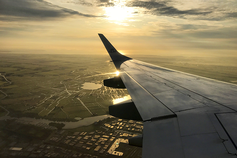 Bilden visar en flygplansvinge och en soluppgång.