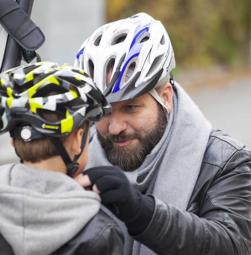 man med cykelhjälm hjälper barn sätta på sig hjälmen