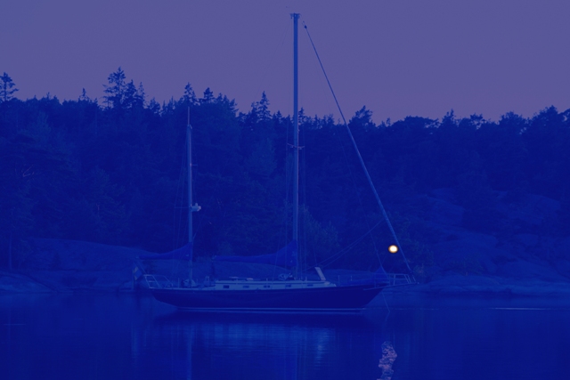 Segelbåt i mörker och ett litet utmärkande ljus, fotografi